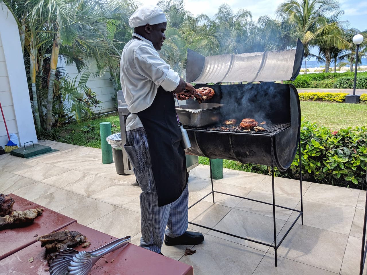 Jamaica Chef grilling meat on an outdoor barbecue.