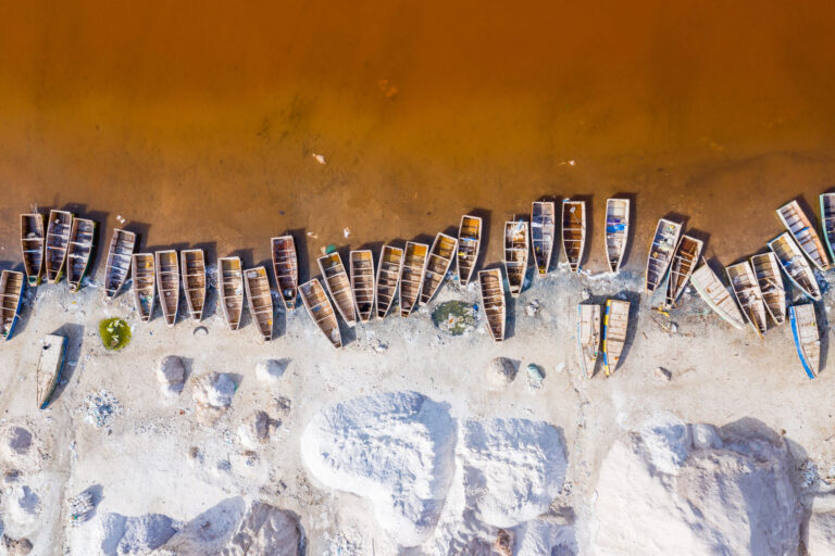 Aerial view of wooden boats along a rust-colored lakeshore with white salt mounds
