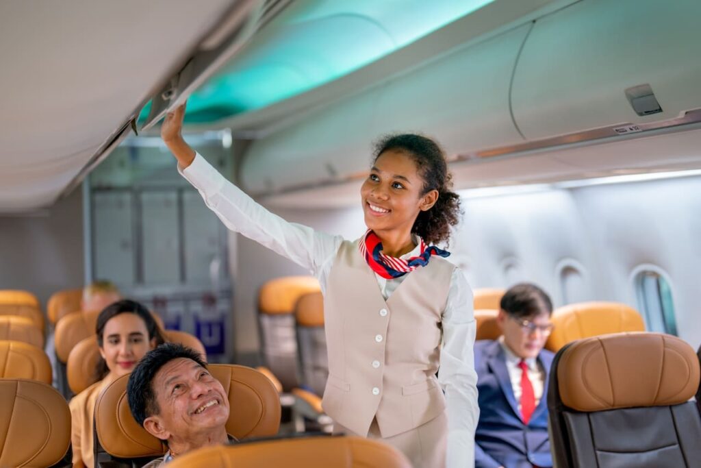 Flight attendant smiling while assisting passengers inside an airplane cabin.